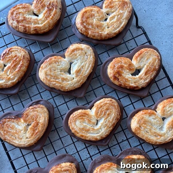 Heart-shaped puff pastries partially dipped in chocolate, arranged on a cooling rack over a gray surface.