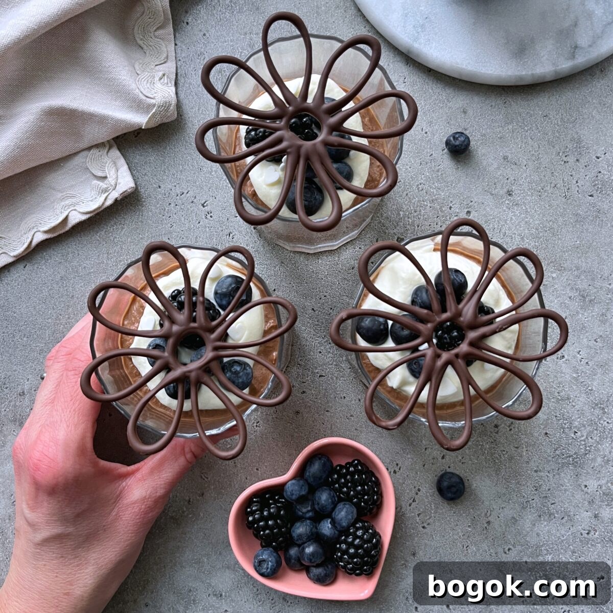 Three dessert glasses filled with chocolate mouse, whipped cream, berries, and decorative chocolate.