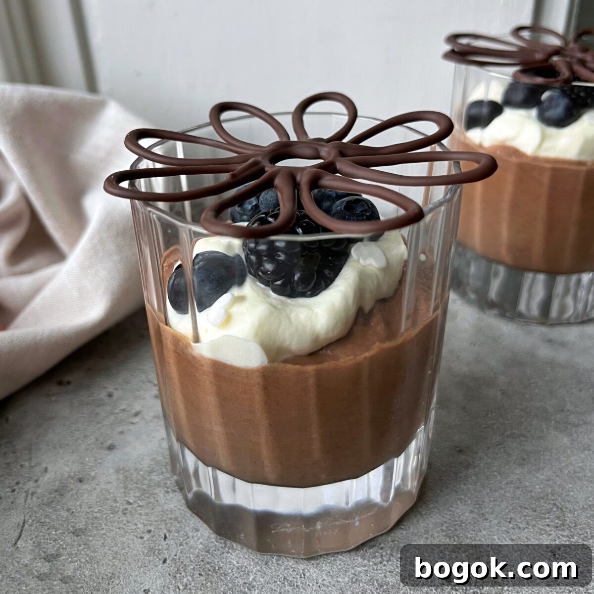 A glass cup filled with chocolate mousse, topped with whipped cream, blueberries, berries, and a decorative chocolate piece.