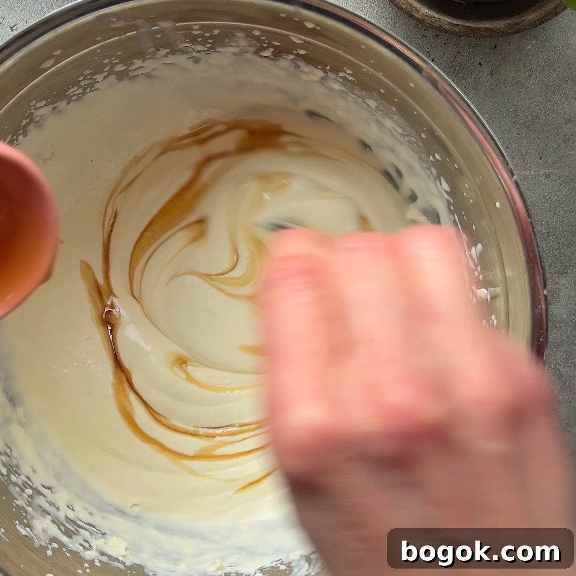 A hand stirs maple syrup into mascarpone whipped cream.