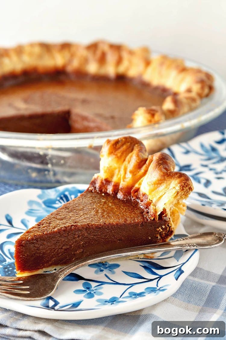 A slice of chocolate caramel buttermilk pie on a blue plate with the whole pie in the background,