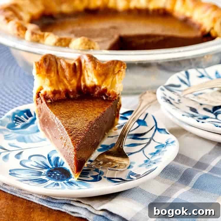 A slice of buttermilk pie on a blue print plate with a silver fork. The rest of the pie in the background.