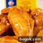 Close up of a flat chicken wing covered in a reddish-orange glaze. An Old Bay seasoning container is out of focus in the background.