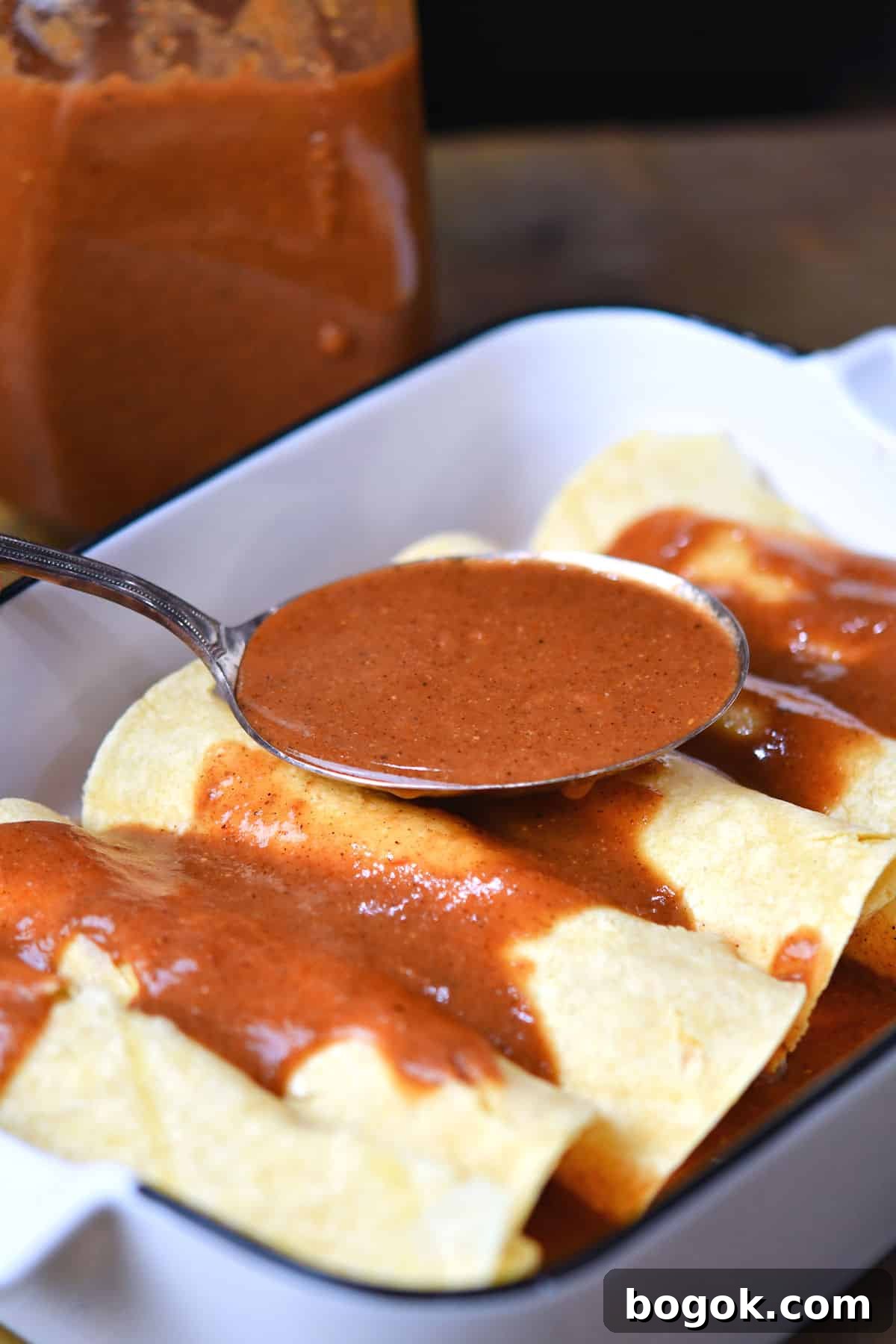 closeup of spooning enchilada sauce over rolled tortillas