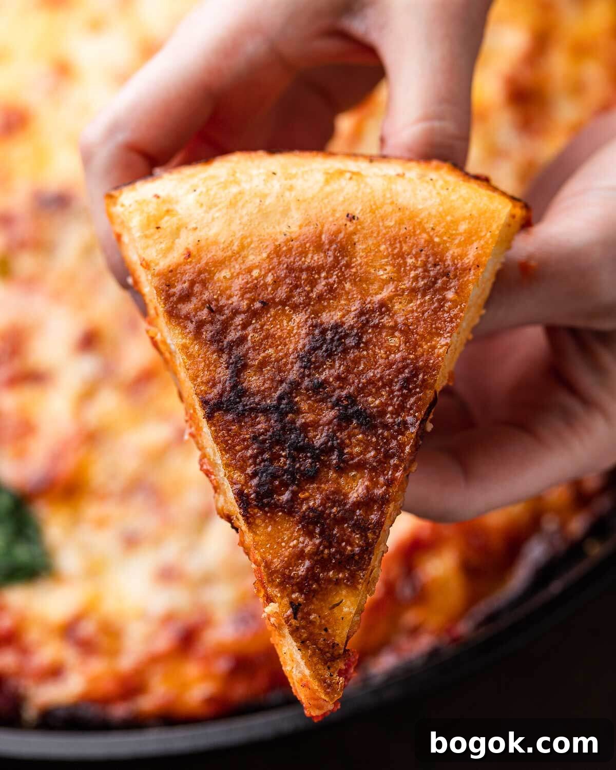 Crispy Cast-Iron Skillet Pizza Recipe 7 Hands holding slice of cast iron pizza turned over to show the golden bottom.