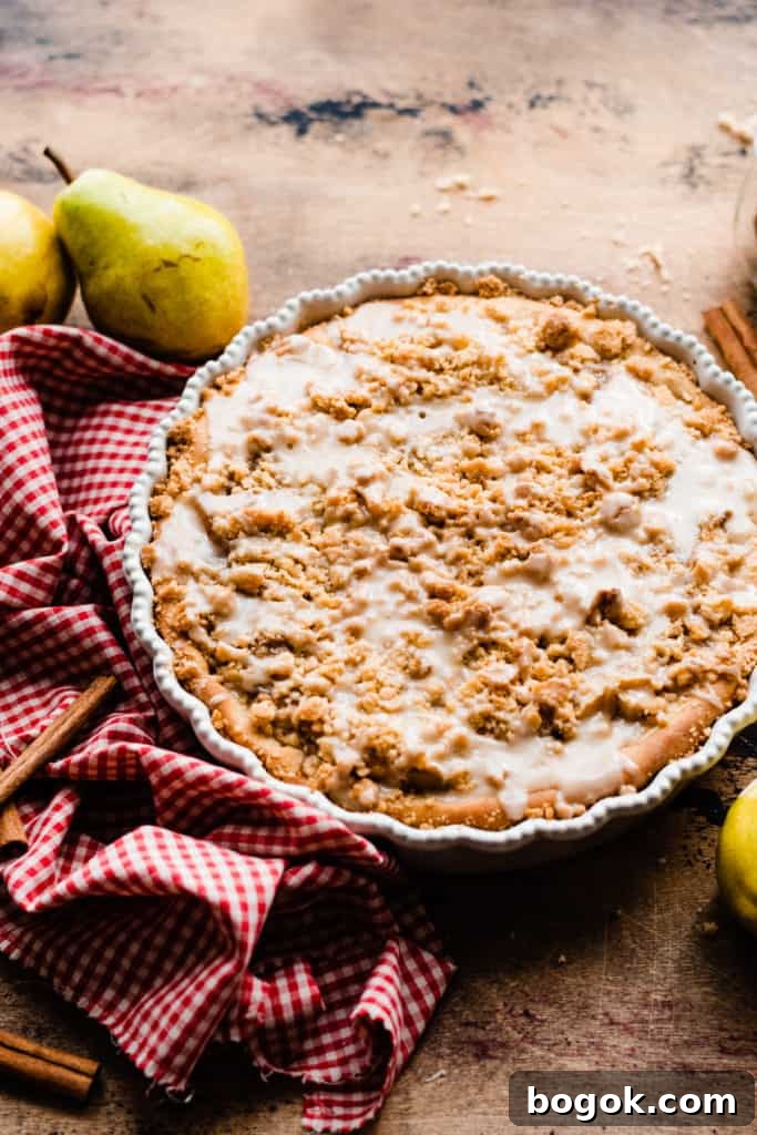A deep dish pear pizza drizzled with glaze, on a wooden surface with a red checked linen and fresh pears