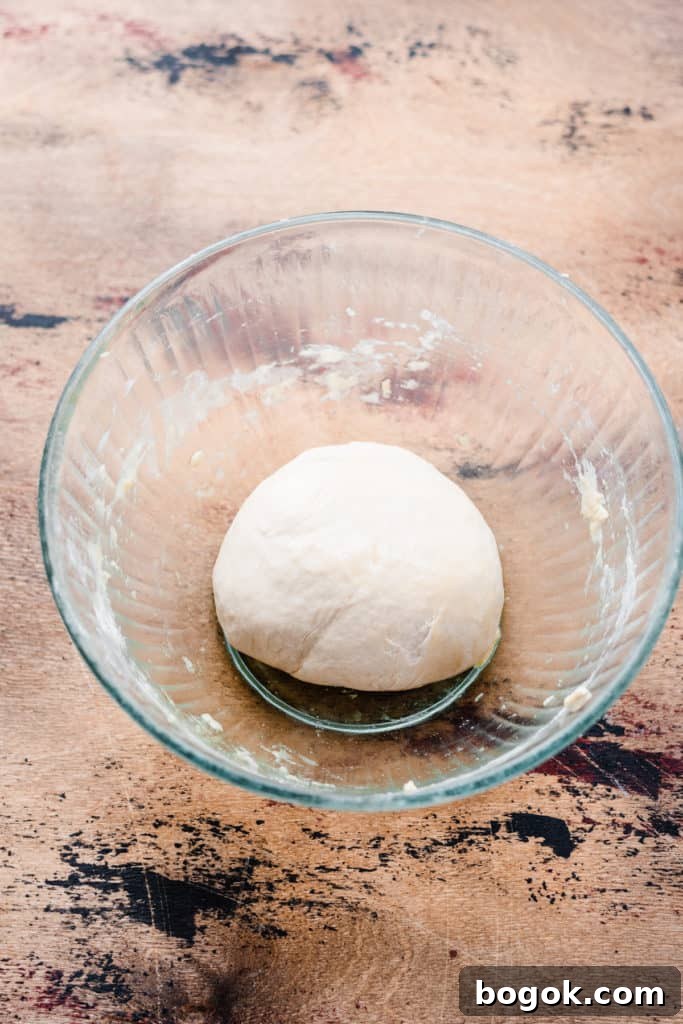 A glass bowl with unrisen pizza dough on a wooden surface