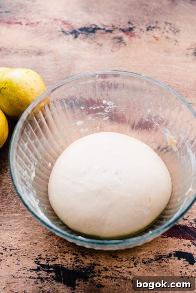 Risen pizza dough in a glass bowl on a wooden surface