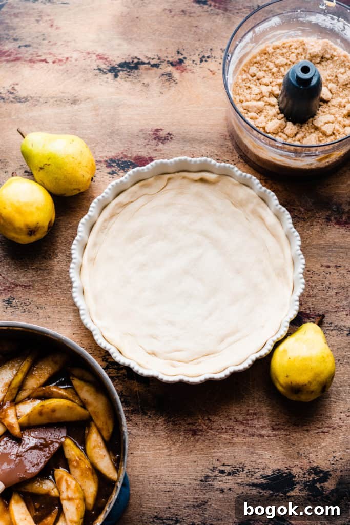 A pie dish with the pizza crust pressed in on a wooden surface, surrounded by fresh pears