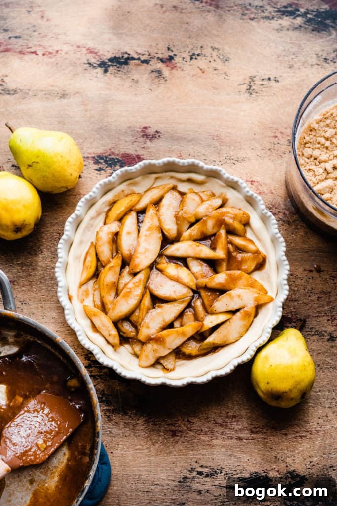A pie dish with the pizza crust pressed in and the pear filling added, on a wooden surface, surrounded by fresh pears