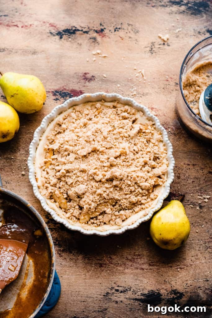 A pie dish with the assembled, unbaked pizza on a wooden surface surrounded by fresh pears