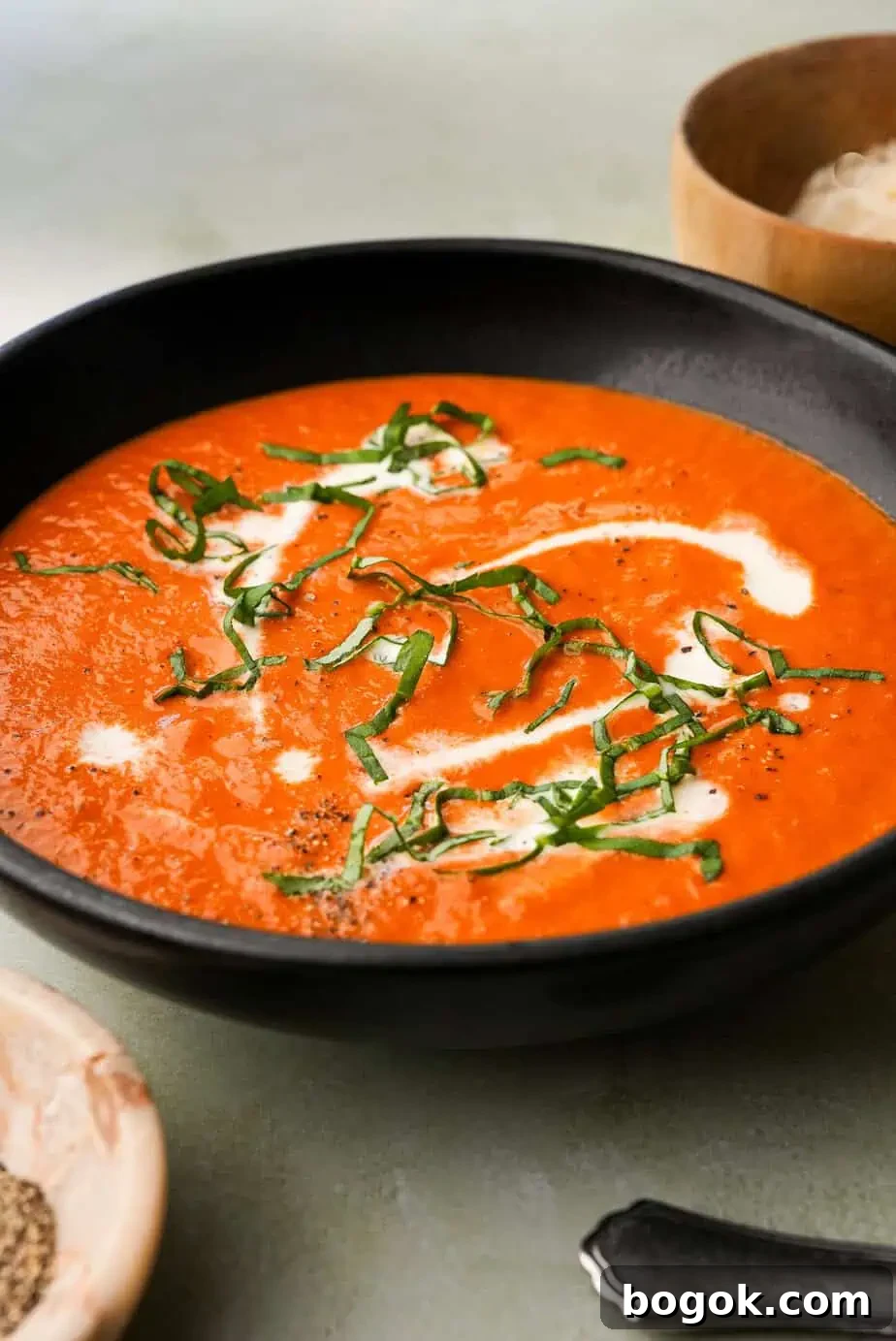A creamy bowl of tomato bisque topped with freshly cracked black pepper and served with a golden, topped with fresh basil, pepper and cream