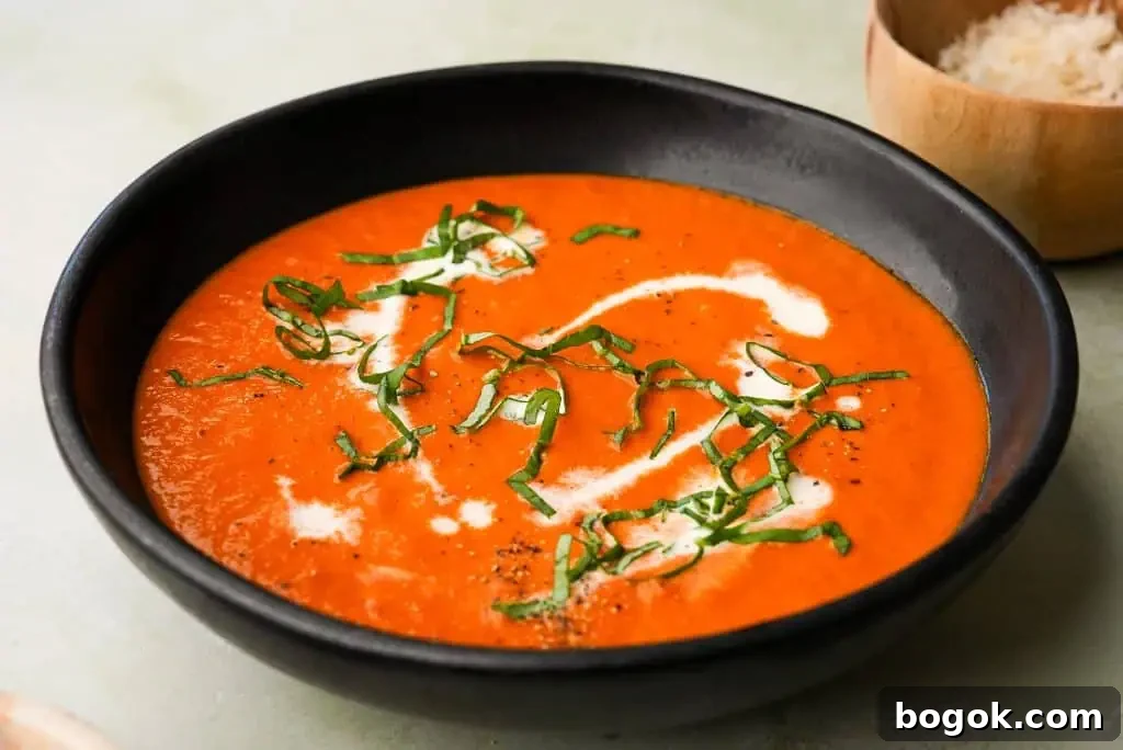 A creamy bowl of tomato bisque topped with freshly cracked black pepper and served with a golden, topped with fresh basil, pepper and cream