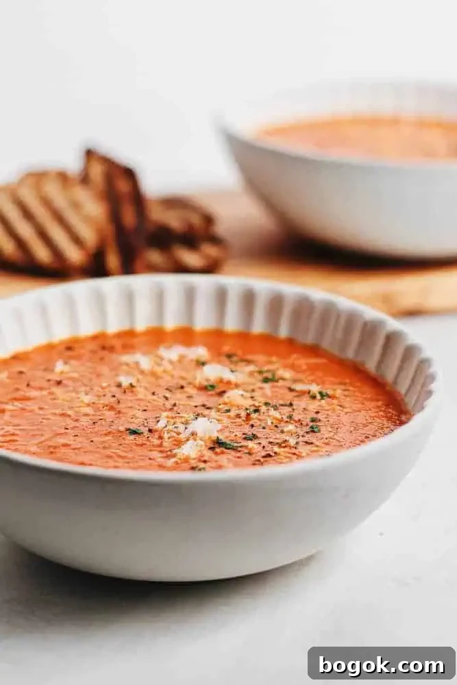 Creamy tomato bisque garnished with grated parmesan and cracked pepper, with grilled bread slices in the background.