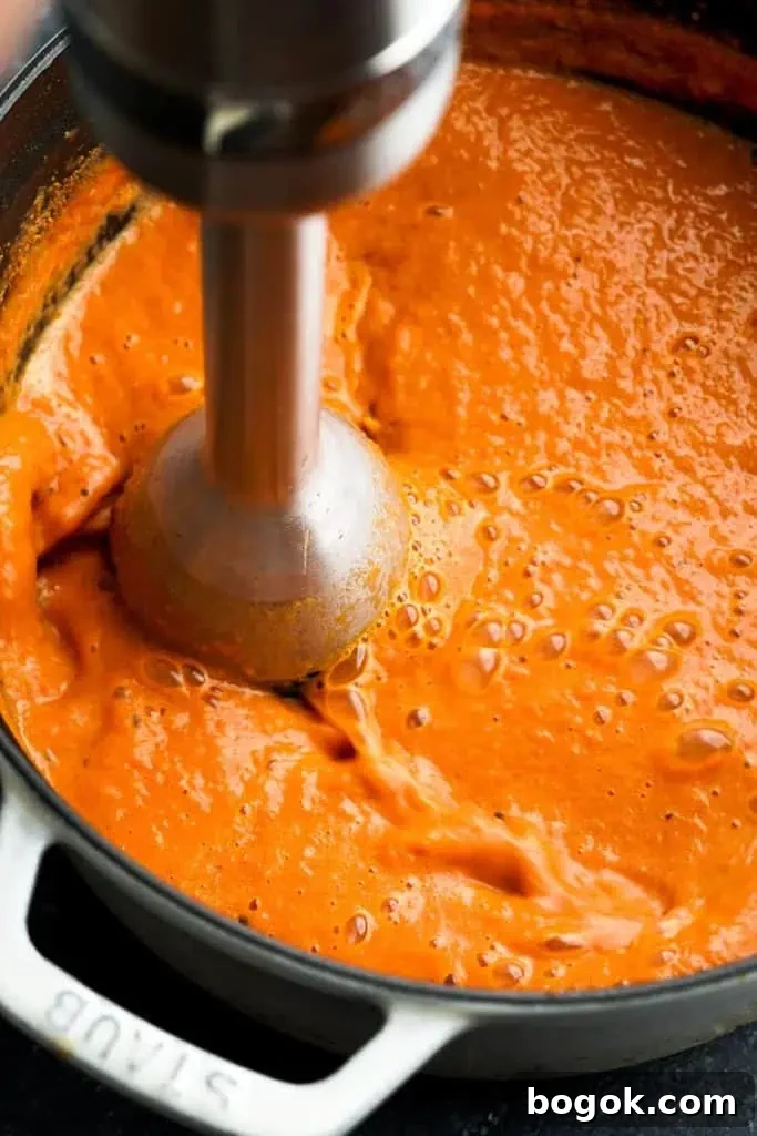 An immersion blender blending tomato bisque in a pot, creating a smooth, creamy texture.