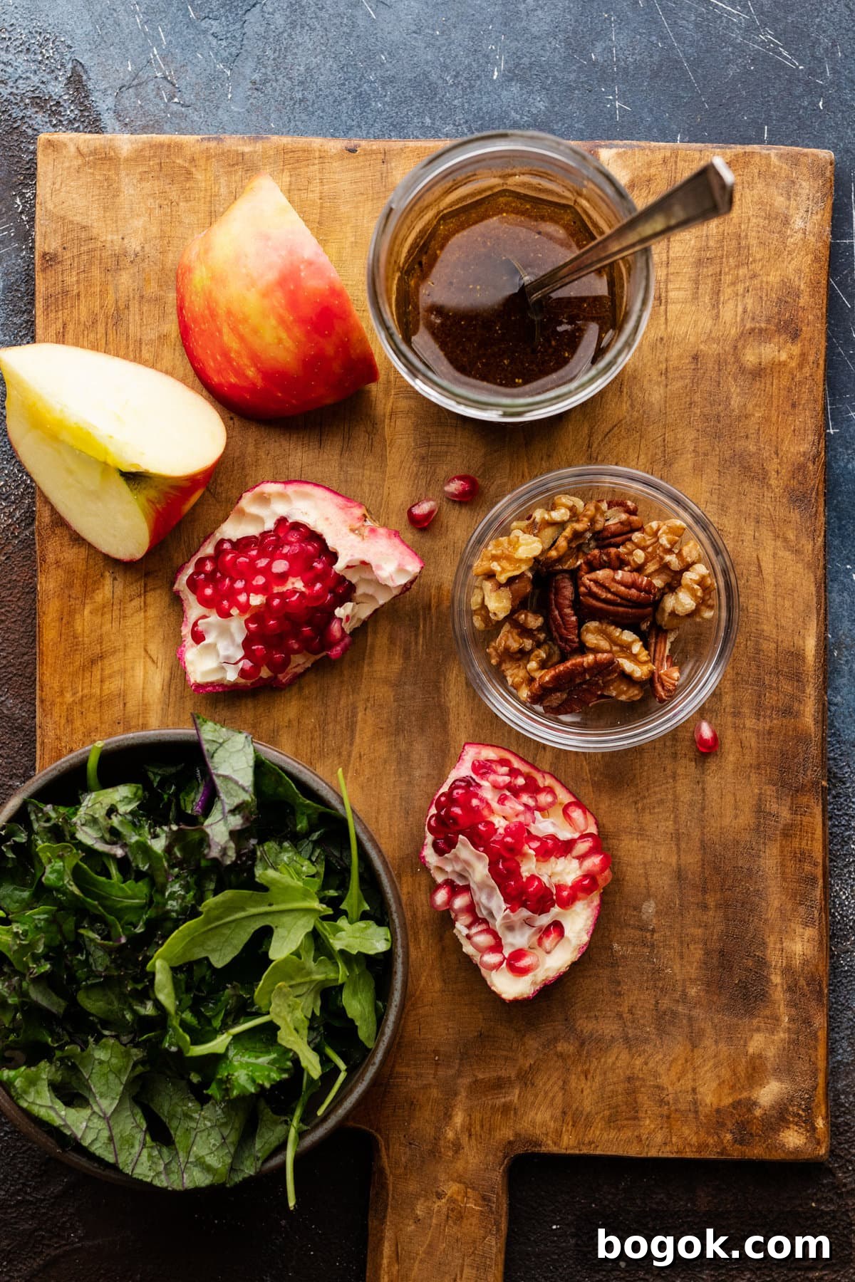 Ingredients for apple pomegranate salad arranged on a brown wooden cutting board.
