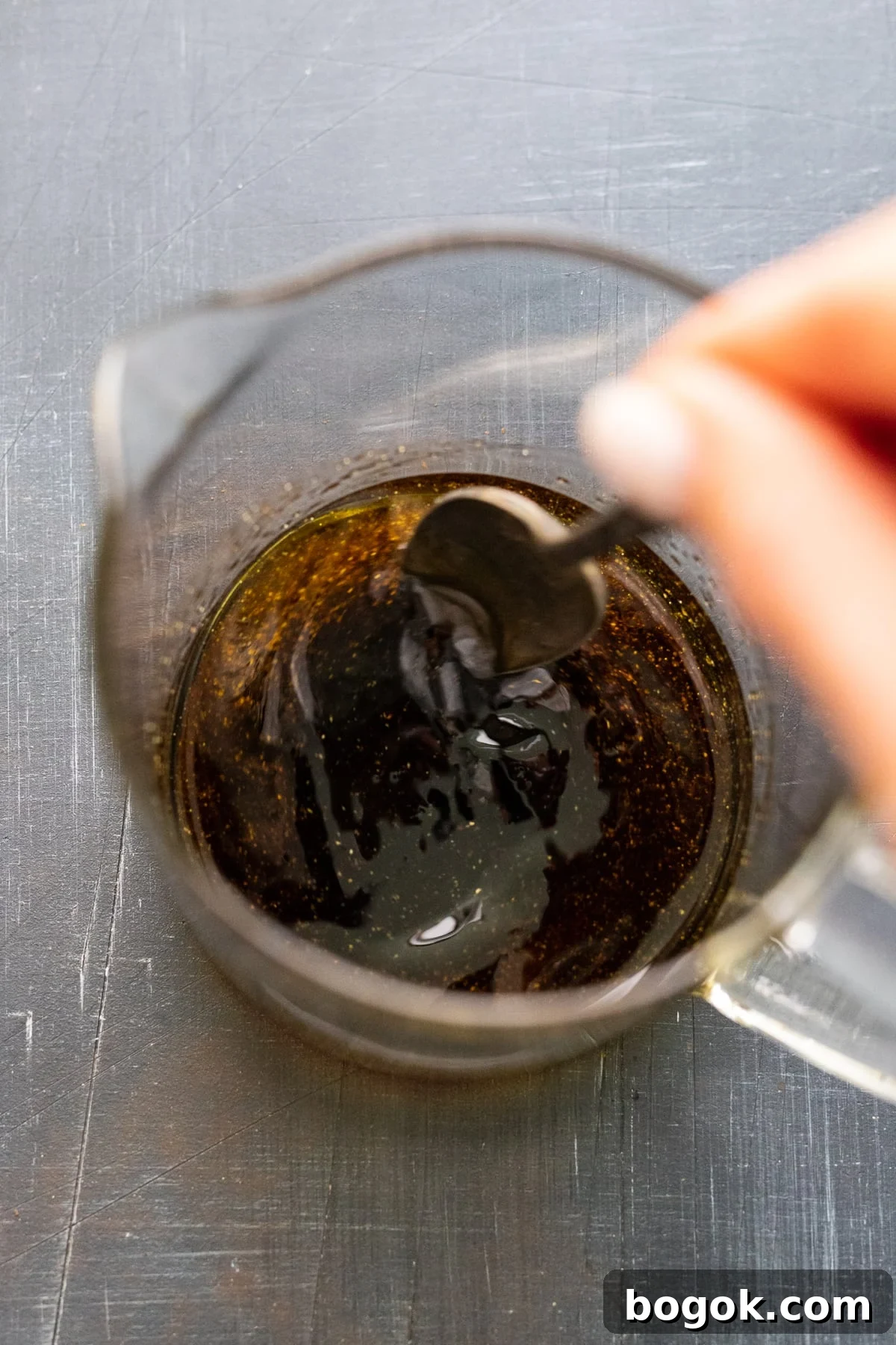 A hand using a spoon to stir balsamic vinegar dressing in a liquid measuring cup.