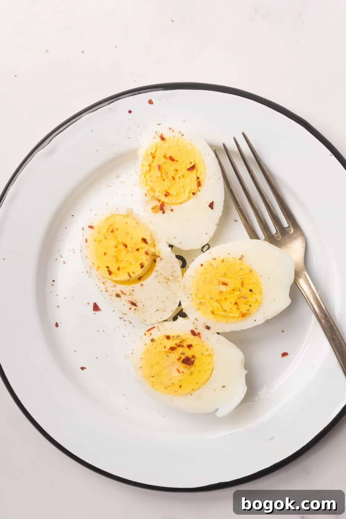 Microwave Method for Perfect Hard-Boiled Eggs in Minutes 2 An image of two hard boiled eggs sliced in half, topped with seasonings, and being served on a plate with a fork beside them.