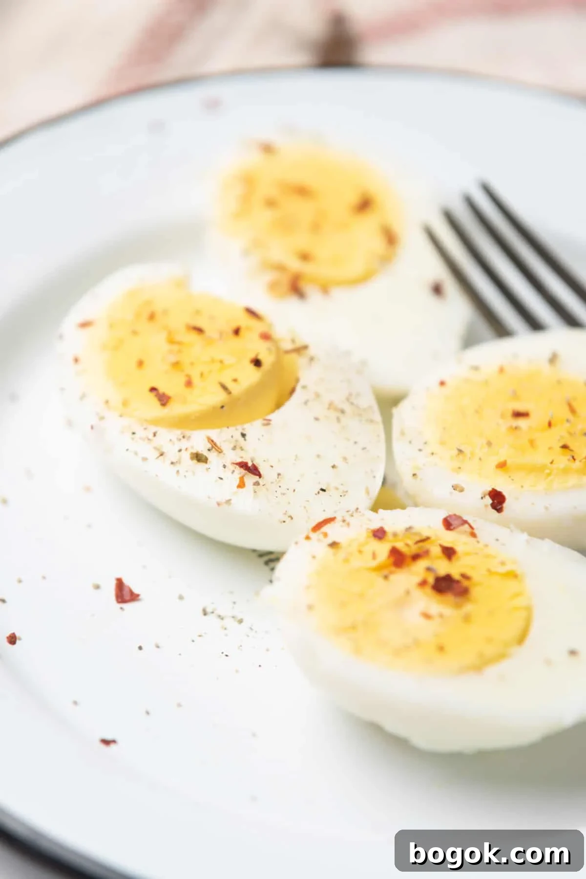 Microwave Method for Perfect Hard-Boiled Eggs in Minutes 4 An image of two hard boiled eggs sliced in half, topped with seasonings, and being served on a plate with a fork behind them.