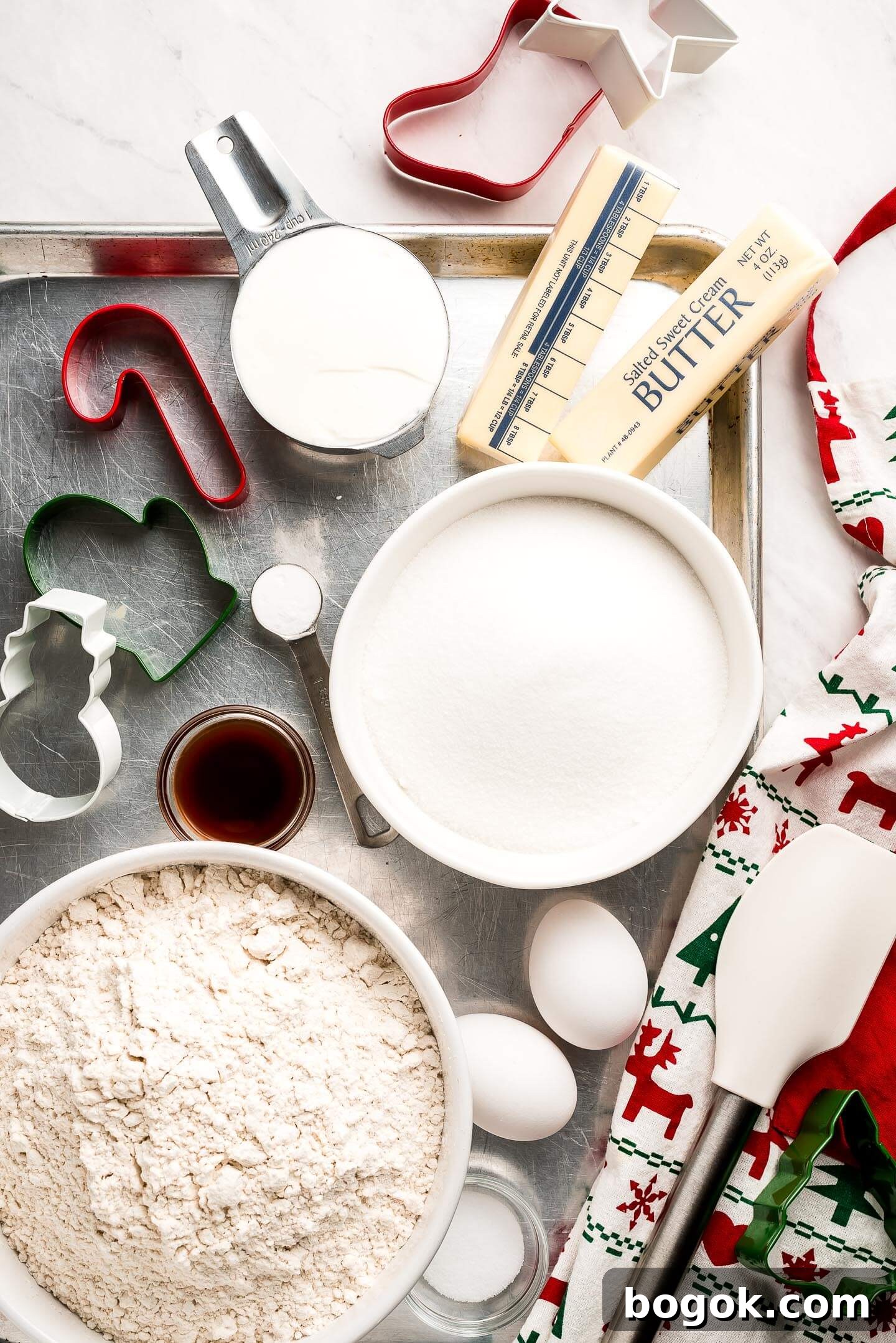 Christmas Sugar Cookie Recipes for Festive Decorating and Gifts 4 A baking sheet with bowls of sugar, flour, eggs, sour cream, sticks of butter, vanilla, and cookie cutters.