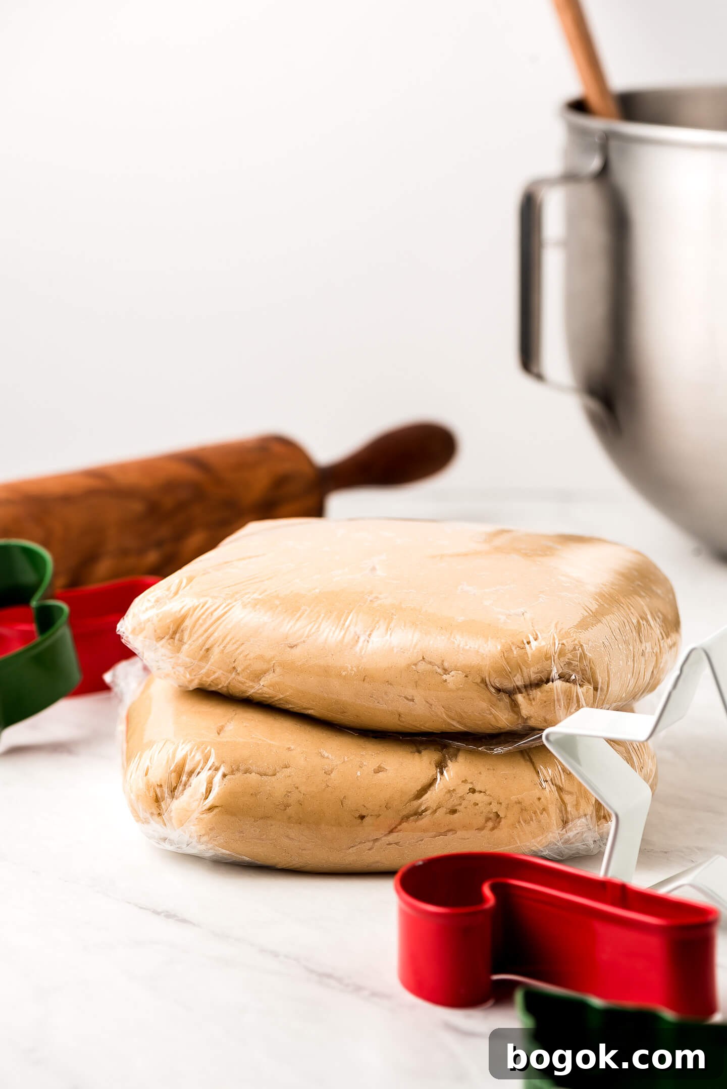Christmas Sugar Cookie Recipes for Festive Decorating and Gifts 6 Rounds of dough in plastic wrap with cookie cutters, a rolling, pin, and mixing bowl in the background.