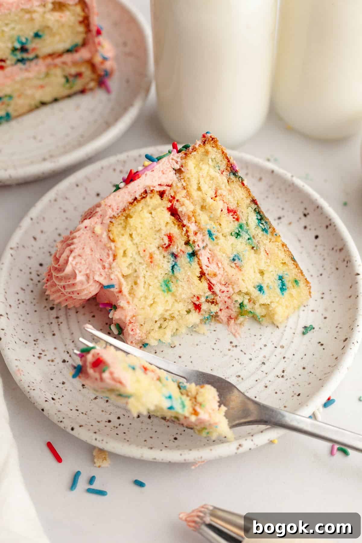 A slice of strawberry funfetti cake on a small plate, a bite has been taken out of it.