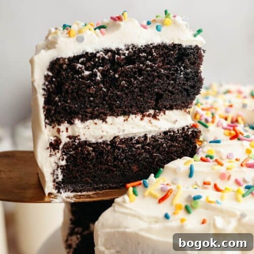 A slice of chocolate cake with vanilla frosting being lifted up with a cake server.