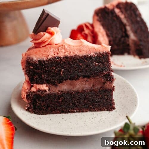 A slice of chocolate cake with strawberry ganache filling and strawberry frosting on a small plate.
