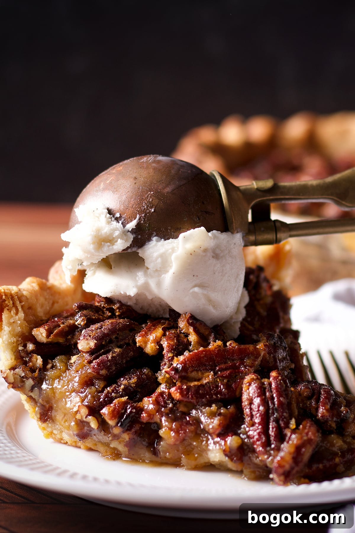 Someone using an old fashioned ice cream scoop to top a slice of pecan pie with vanilla ice cream.