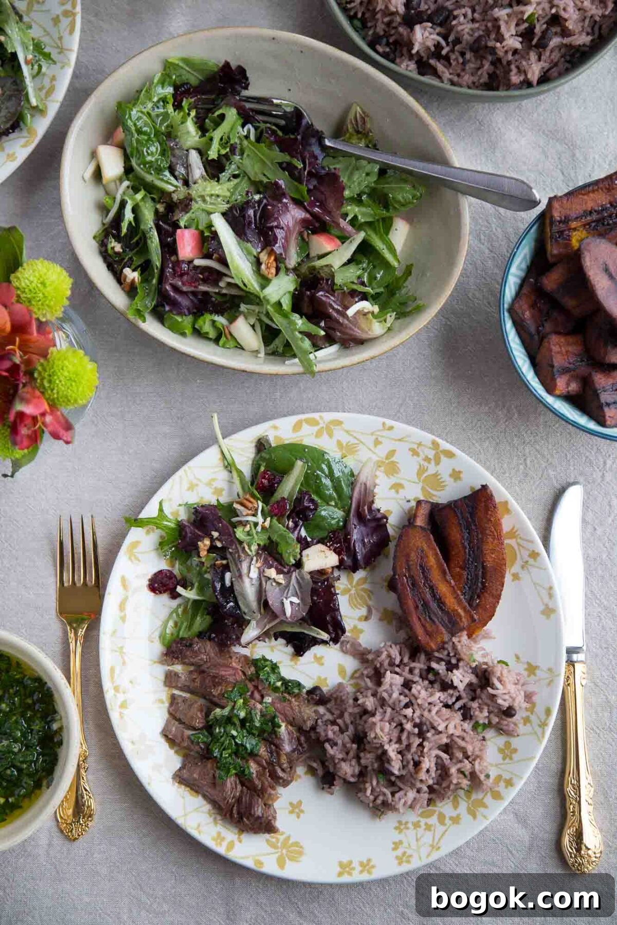 dinner plate with steak, rice, winter fruit salad, and plantains on a dinner table.