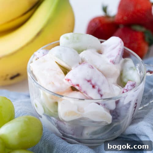 creamy fruit salad in a glass dish, surrounded by fresh fruit.