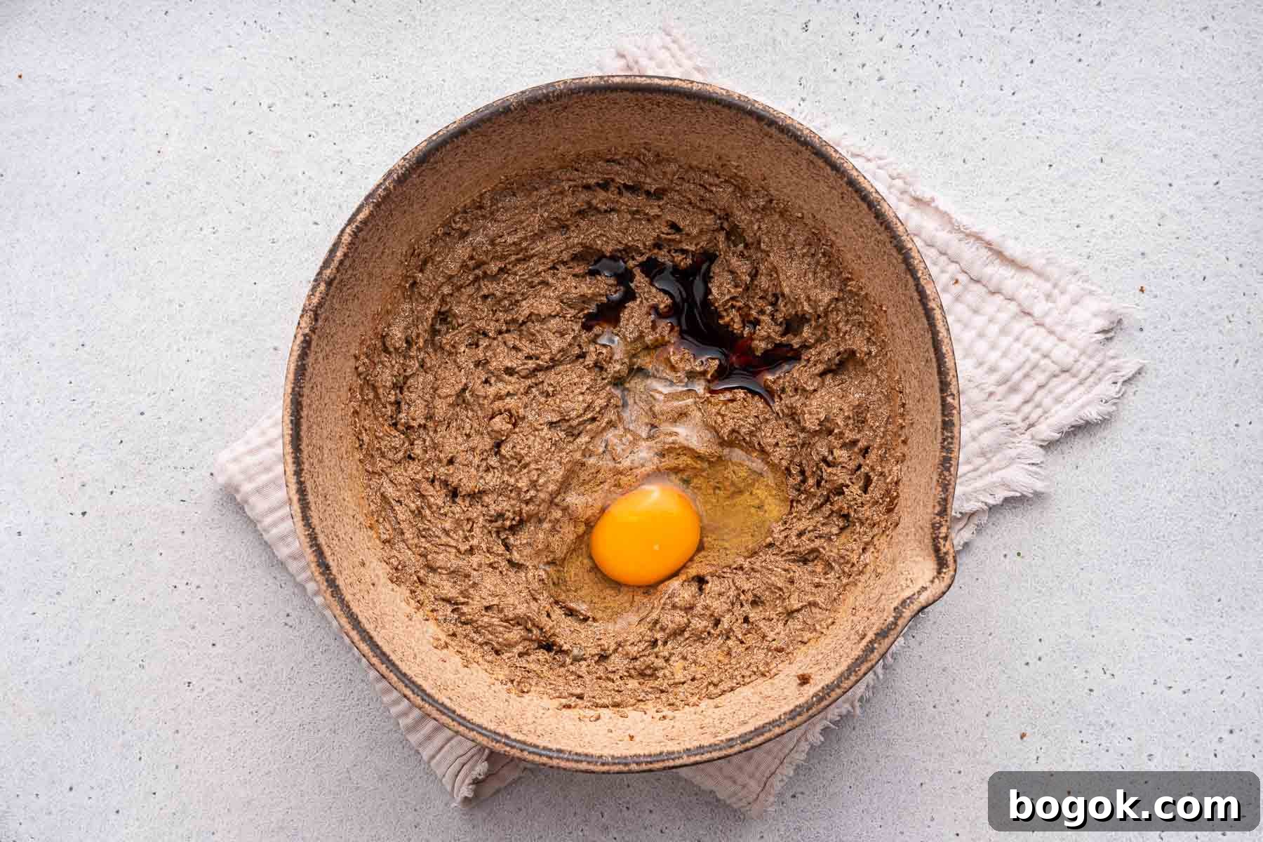 Egg and vanilla on top of brown batter in a brown mixing bowl.