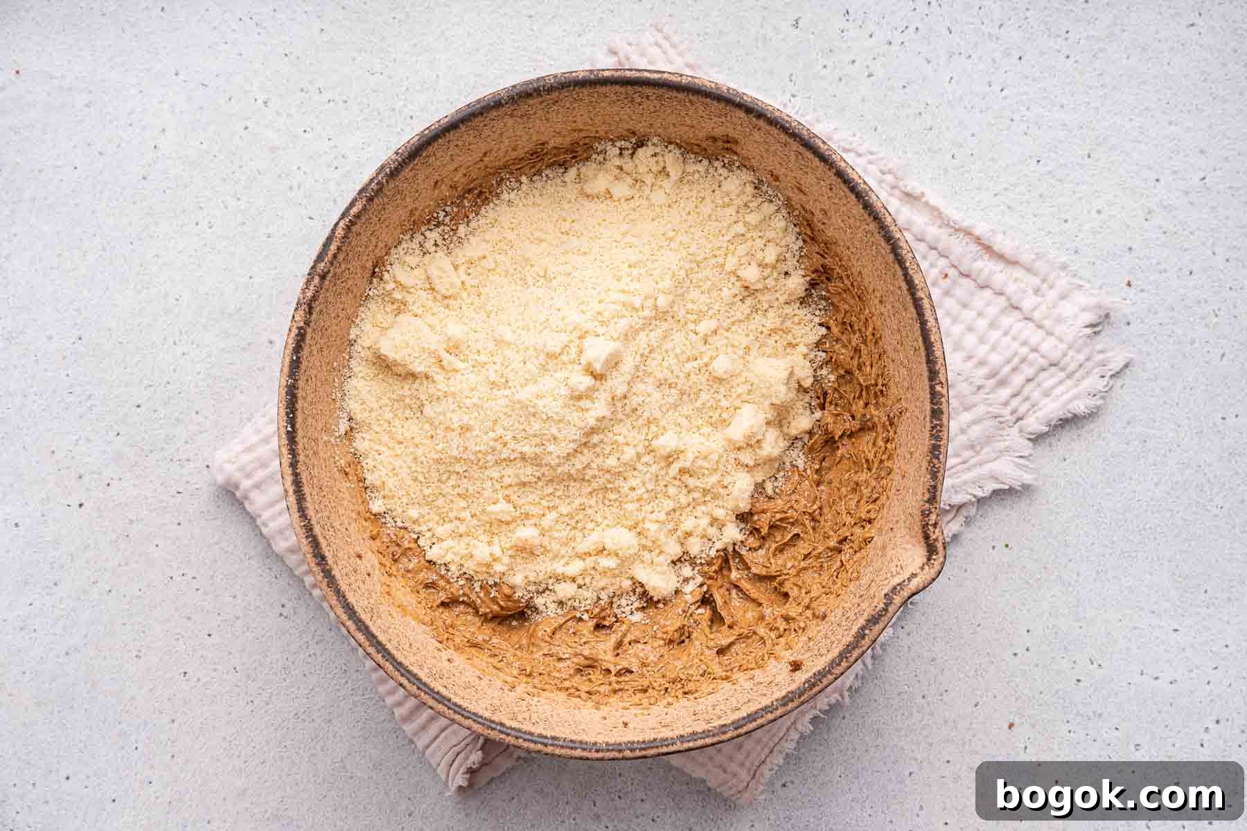 Adding yellow flour on top of raw brown cookie dough in mixing bowl.