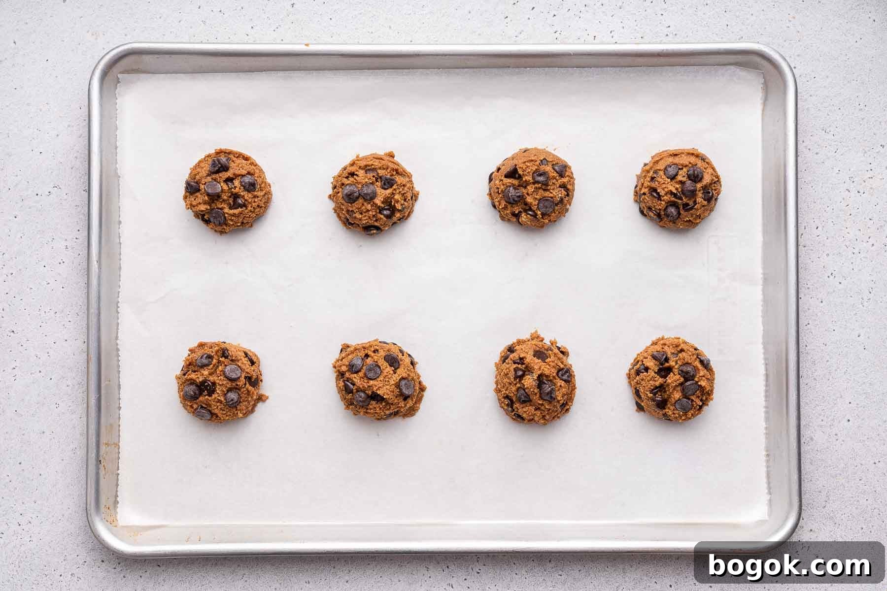 Eight almond flour chocolate chip cookie spaced out on a baking sheet, before baking. 