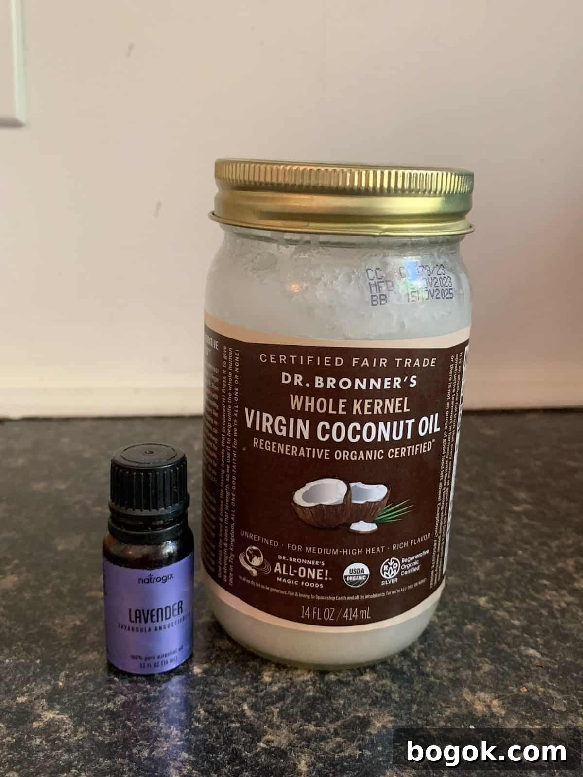 A large jar of Dr. Bronner's Virgin Coconut Oil sits next to a small bottle of lavender essential oil on a dark countertop.