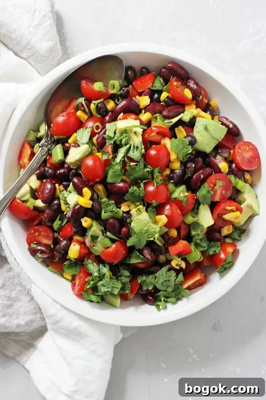 This easy mexican bean salad can be made in advance and is delicious served cold or at room temp! Excellent for BBQs, potlucks and picnics! Filled with two kinds of beans, crunchy veggies and creamy avocado! And finished with a fantastic lime chipotle dressing. A white bowl filled with Mexican Black Bean Salad with a silver serving spoon in the dish.