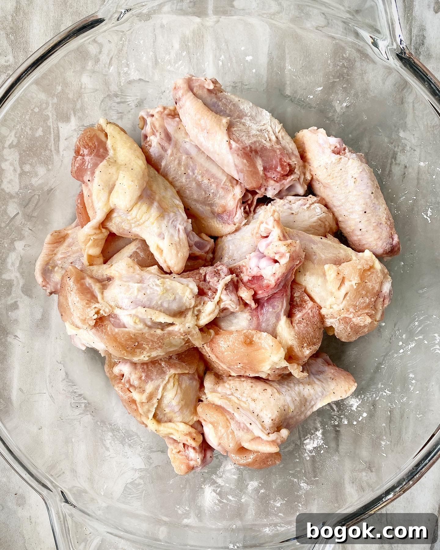 raw chicken wings in a clear bowl seasoned with salt, pepper, and arrowroot flour