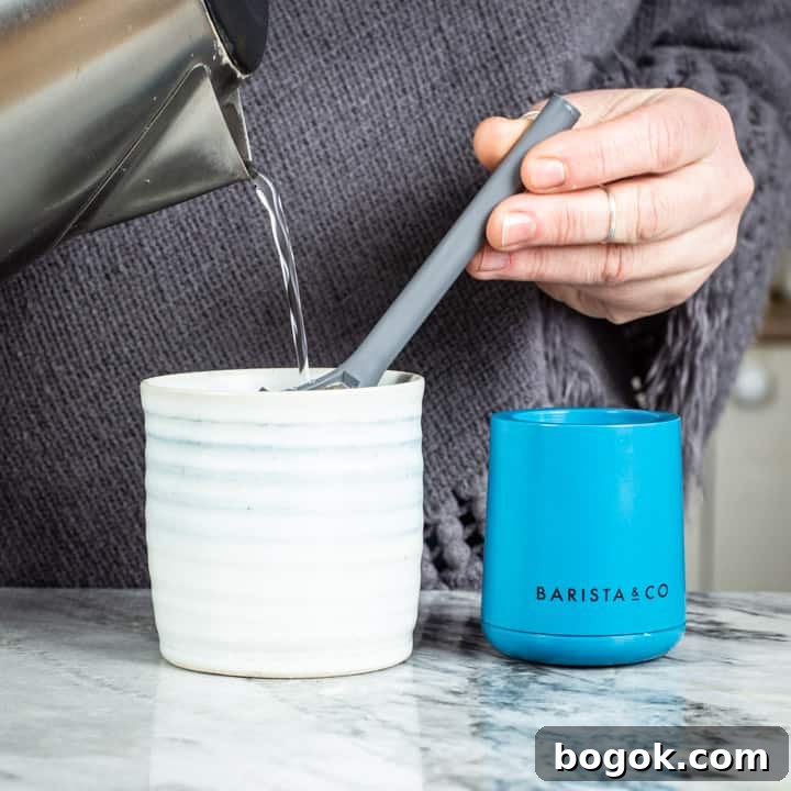 womans hands pouring water from a kettle into the brew it stick coffee maker into a handmade mug on a marble surface