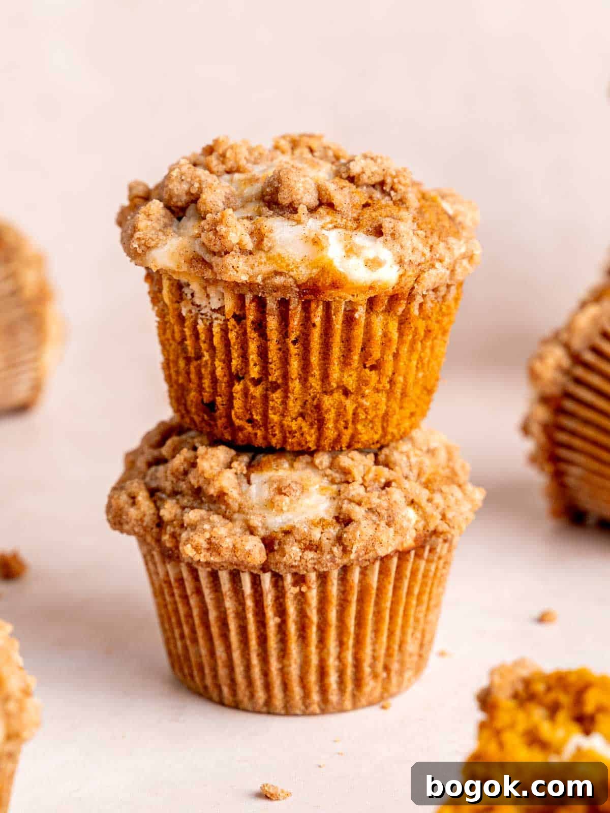 Two pumpkin cheesecake muffins with streusel stacked on top of each other.
