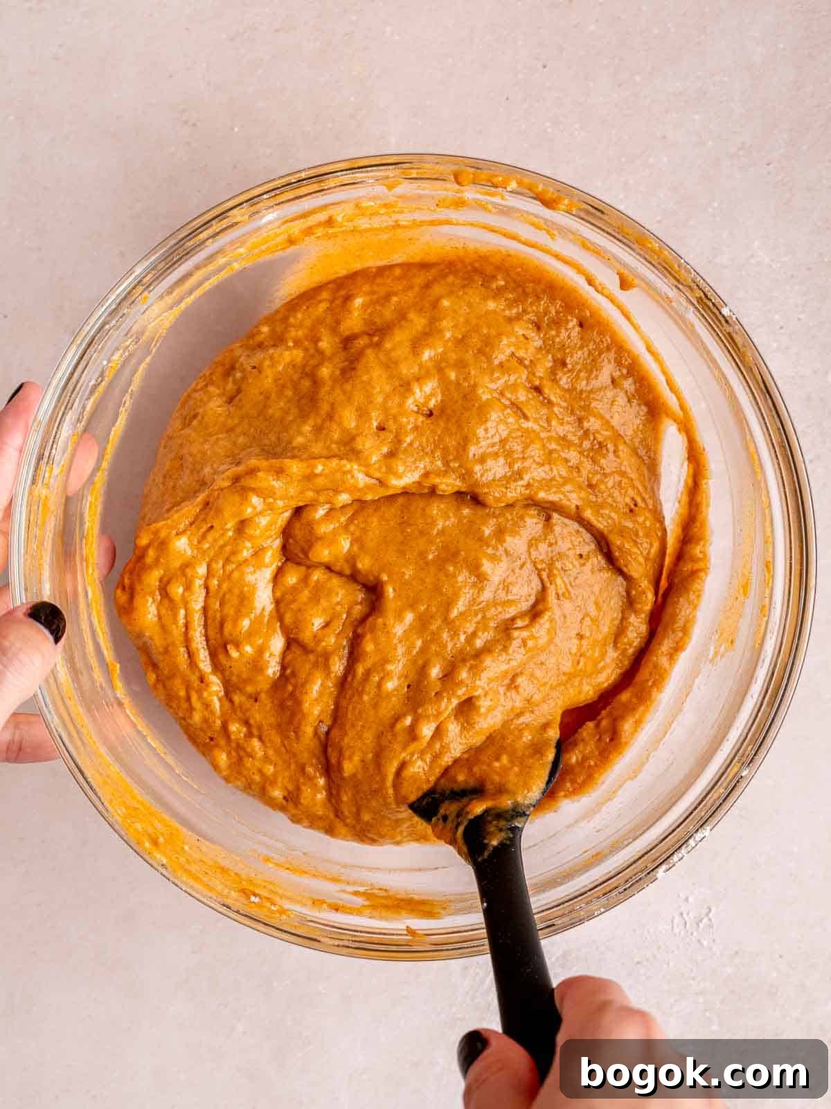 Folding pumpkin muffin batter in a bowl using a rubber spatula.
