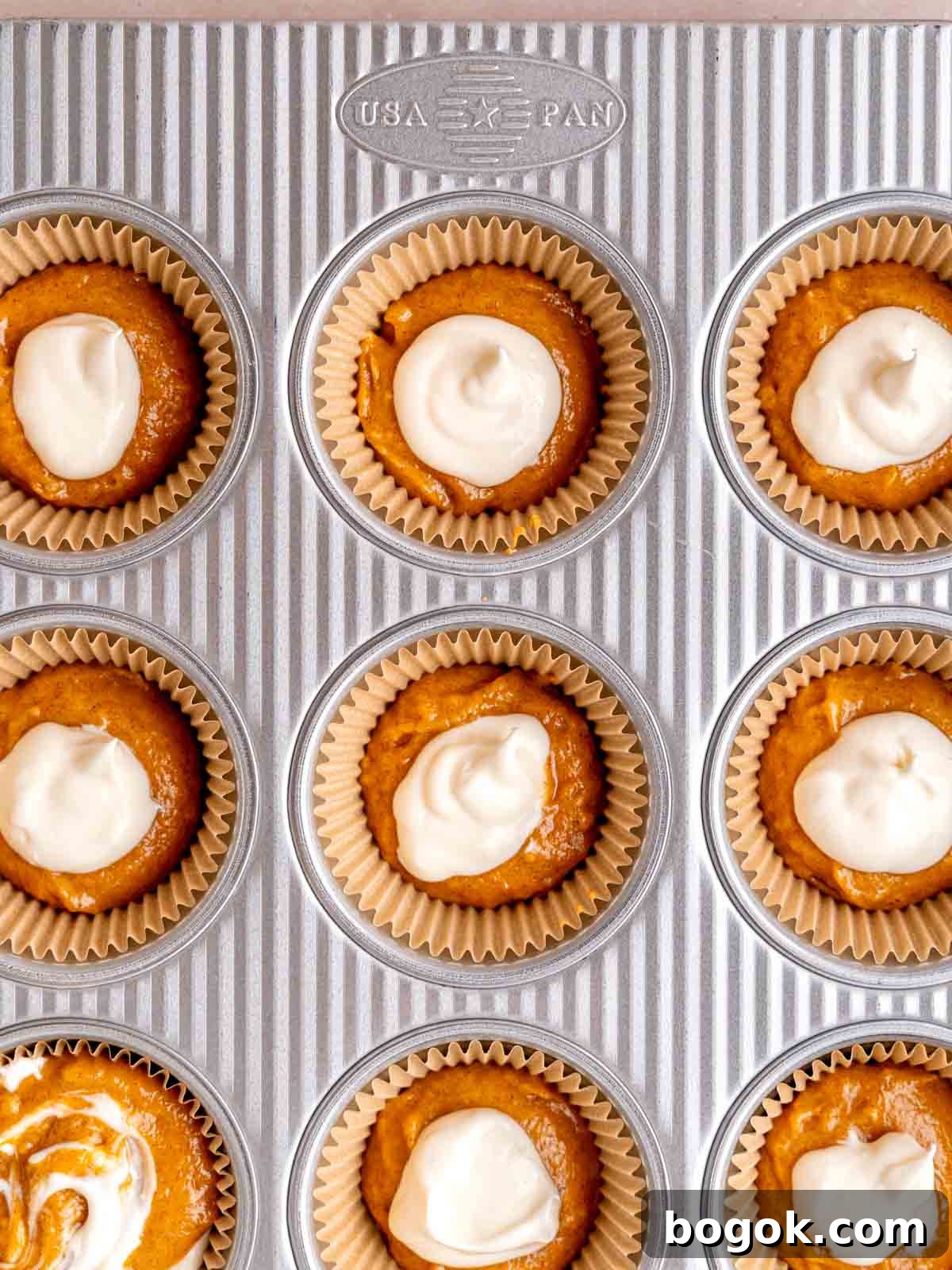 A muffin pan filled with pumpkin batter and cream cheese filling.