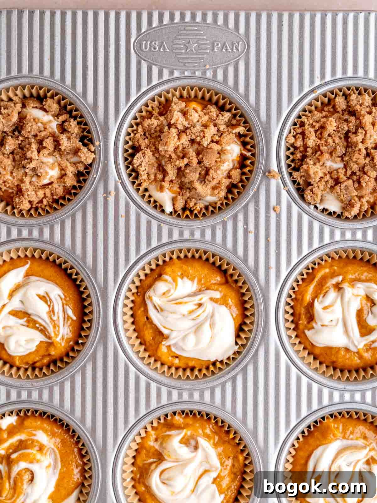 Pumpkin muffin batter with cream cheese and streusel topping in a pan.