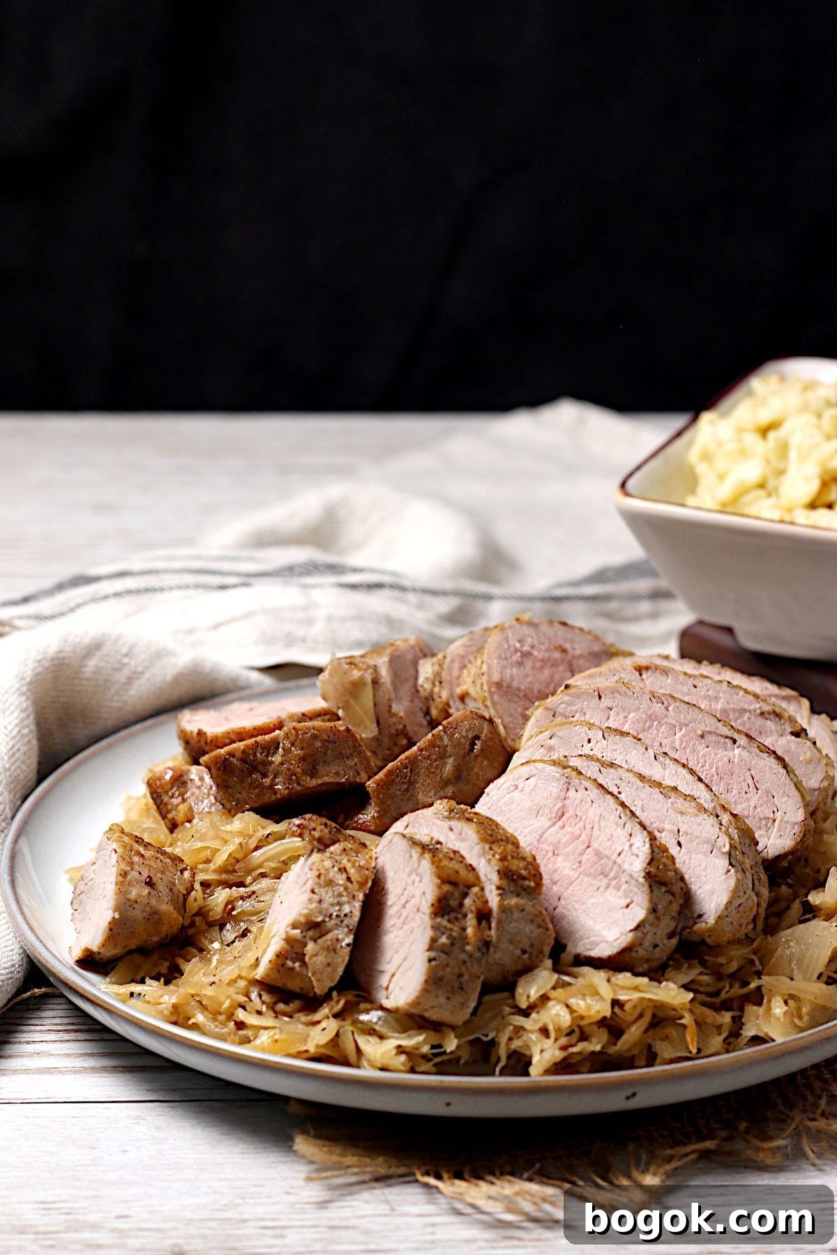 Crispy Roasted Pork Tenderloin with Tangy Sauerkraut 3 Sliced pork tenderloin sitting on a bed of sauerkraut on a large plate.
