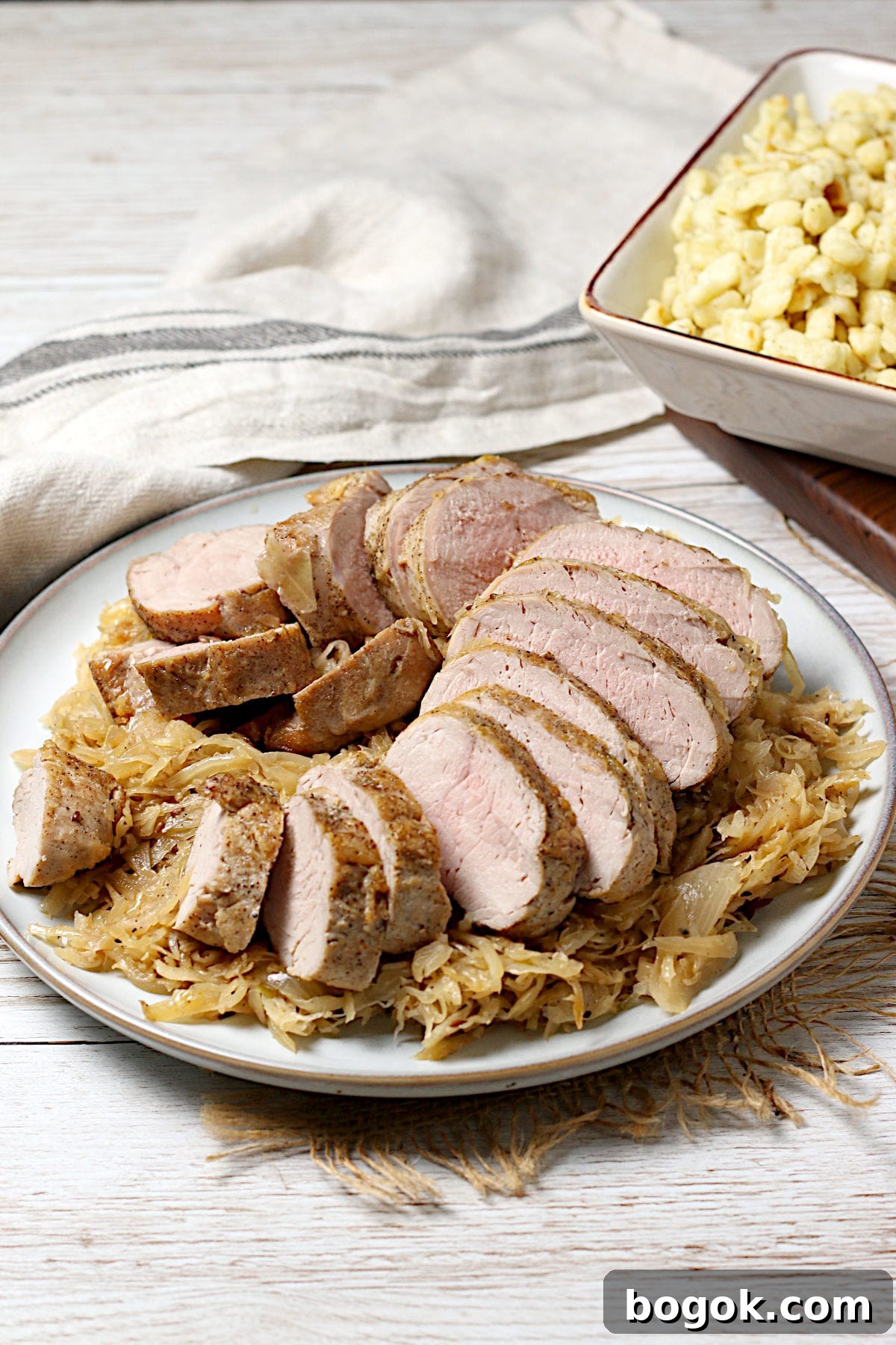 Crispy Roasted Pork Tenderloin with Tangy Sauerkraut 4 Sliced pork tenderloin sitting on a bed of sauerkraut on a large plate.