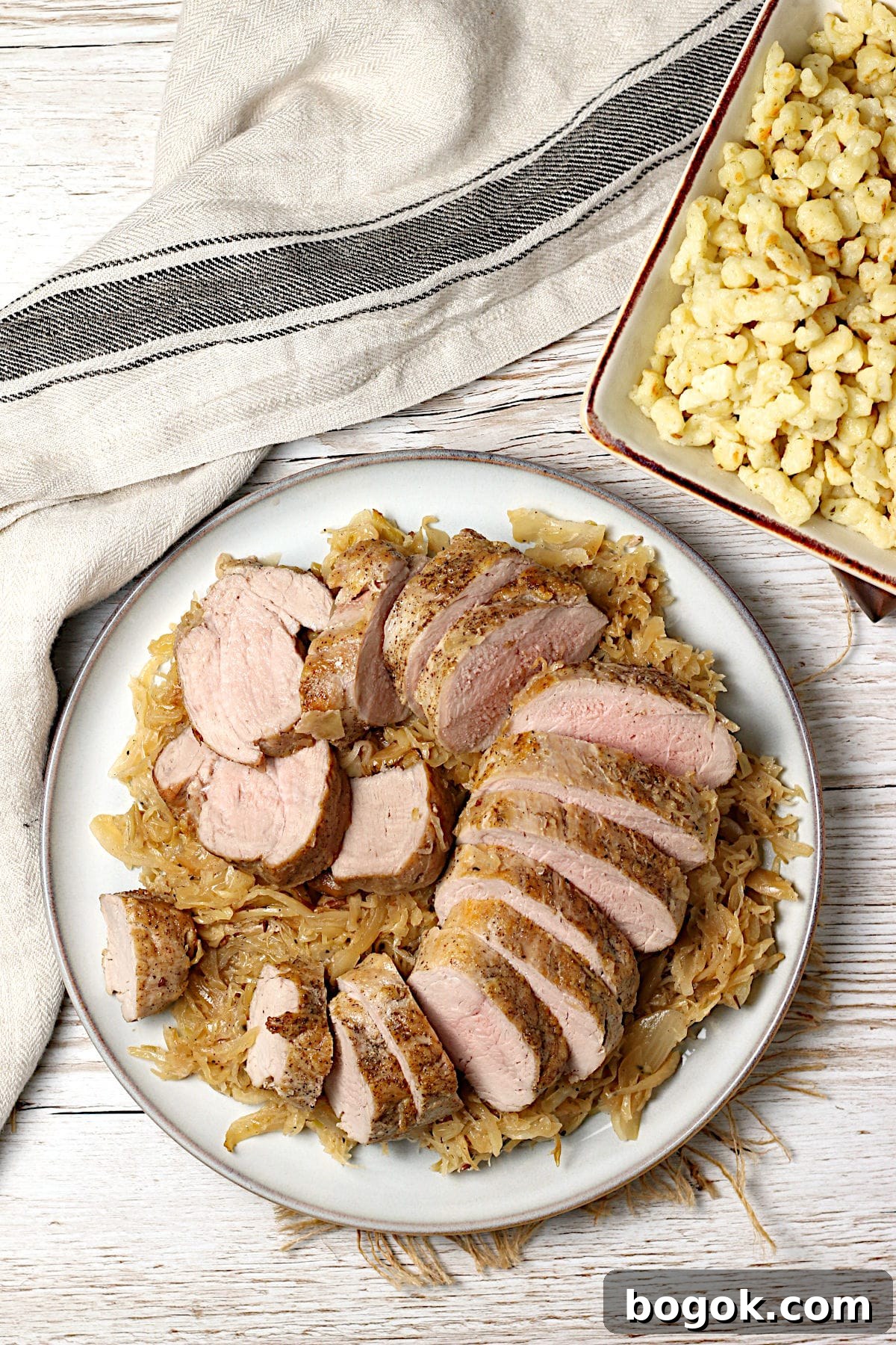 Crispy Roasted Pork Tenderloin with Tangy Sauerkraut 5 Overhead photo of sliced pork tenderloin sitting on a bed of sauerkraut on a large plate.