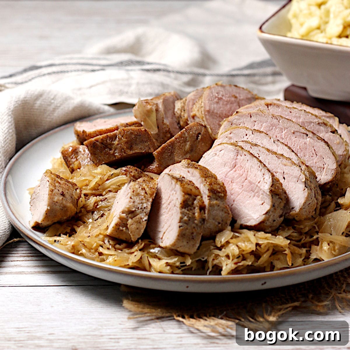 Crispy Roasted Pork Tenderloin with Tangy Sauerkraut 9 Sliced pork tenderloin sitting on a bed of sauerkraut on a large plate.