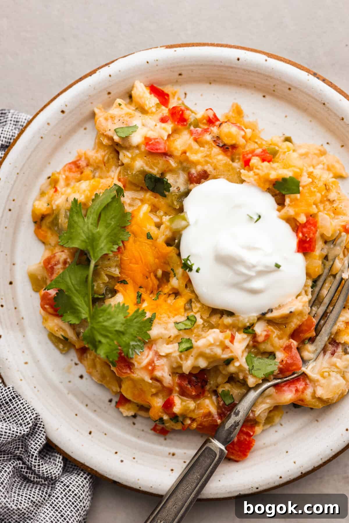 Top view of a serving of king ranch casserole on a plate garnished with cilantro and sour cream.