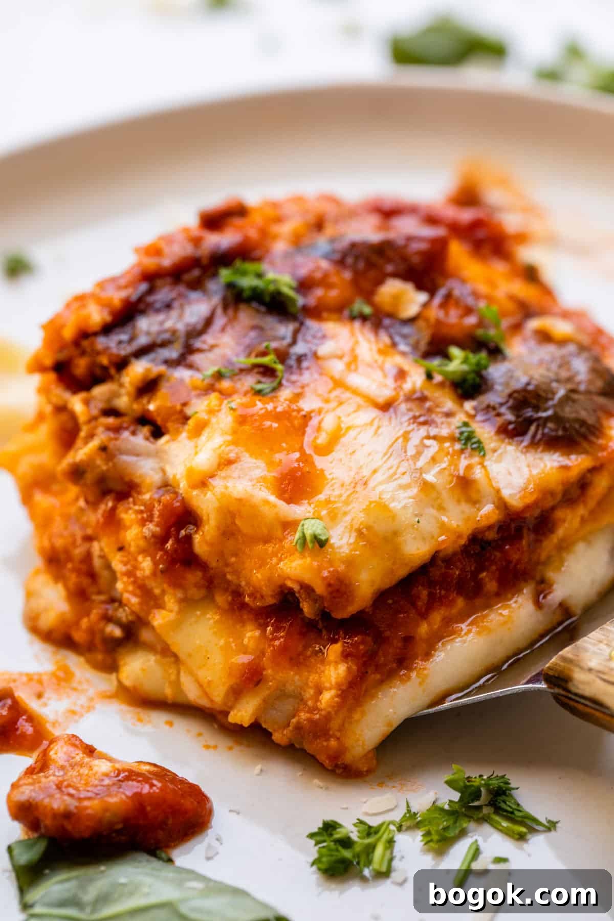 Ultimate Homemade Lasagna Recipe for Savory, Cheesy Layers 12 putting a piece of lasagna on a white plate with a spatula.