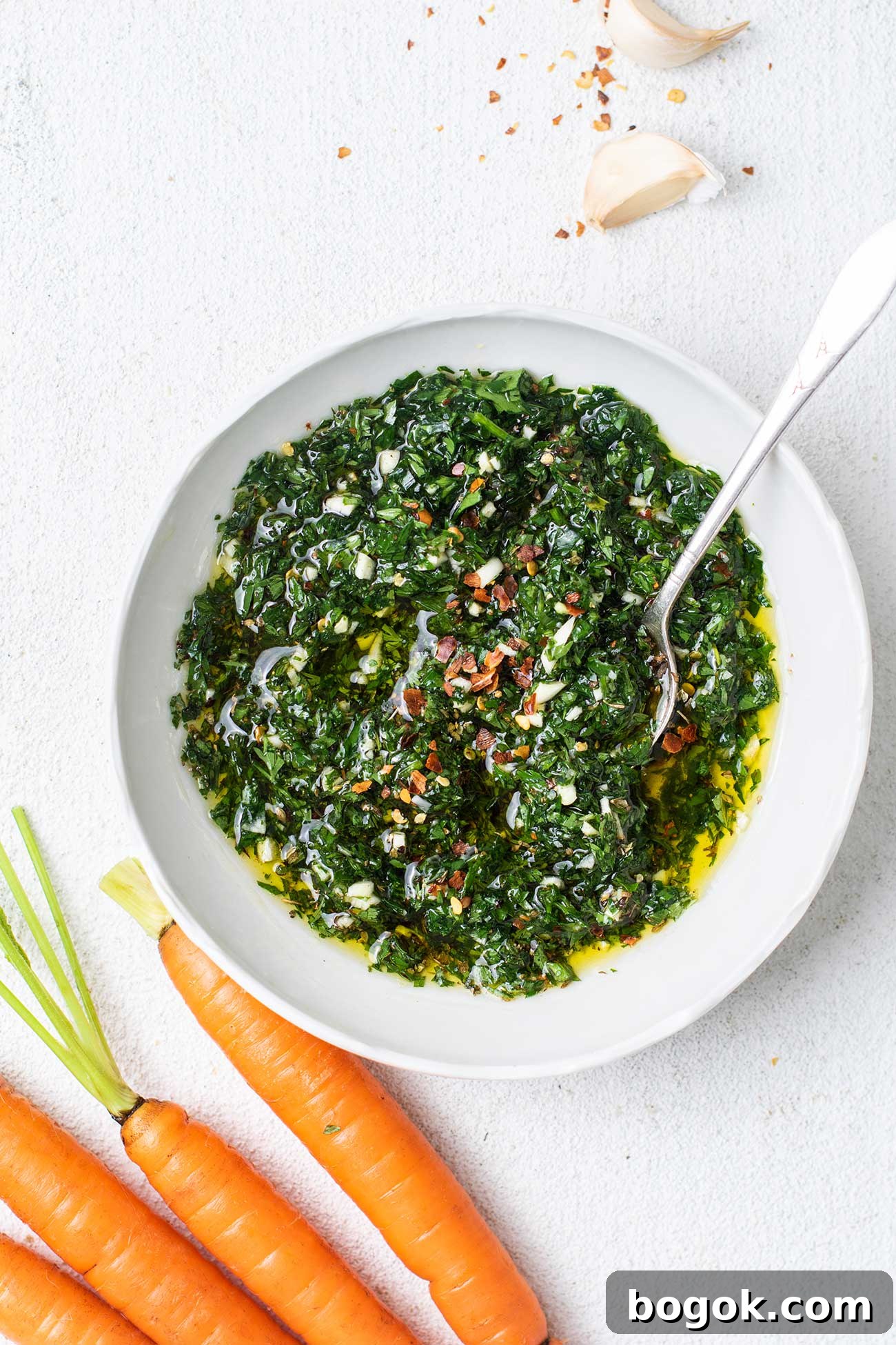 A bowl of carrot top chimichurri shown stirred together and garnished with red chili.