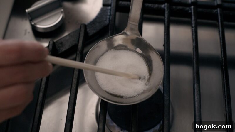 5-Minute Dalgona Candy Recipe: Quick Korean Honeycomb Toffee 7 A wooden chopstick is stirring white sugar in a ladle over low heat on the stove.